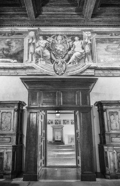 An historic ornate wood framed door with an elaborate fresco above. Through the door is seen a brightly lit outer room. Processed in black and white.