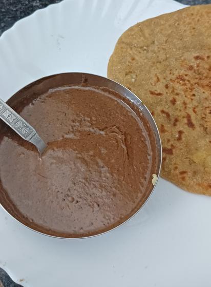 A small katori of dal makhani on white ceramic plate, and one aloo paratha, kept on a white ceramic plate.