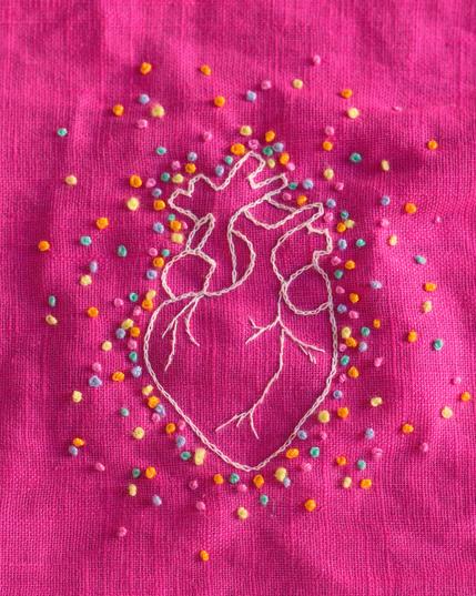 sur un tissu rose vif, broderie d'un cœur anatomique stylisé, avec des points multicolores pastel autour