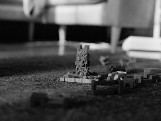 A tiki tree trunk children's toy with a glaring face staring at the camera with game pieces laying around it.