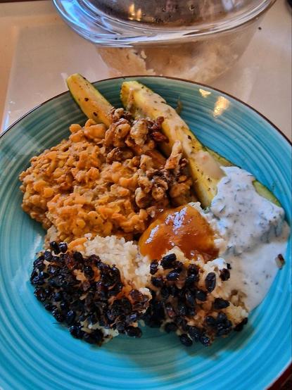 Gelbe Linsen mit Cashews und Berbere, gebratene Zuccini mit Piment, Walnuss und Zitrone, Reis mit Berberizen, Raita mit schwarzem Pfeffer und Minze, Chutney mit Mango.
Auf einem Türkisen Teller