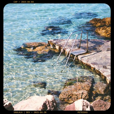 A photo of shallow, clear blue water with a small metal ladder for access, surounded by some rocks