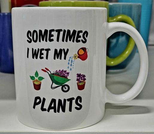 A white coffee mug (handle on the right) on a store shelf. Green and blue mugs in the background.

Black lettering on the mug with a picture of small planters, a filled green wheelbarrow, and a watering pot:

SOMETIMES
I WET MY
<picture>
PLANTS