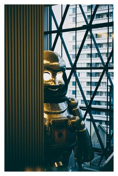 Color photograph taken in a museum in Osaka. It shows a large robot in front of a window, peering out from next to a wall.