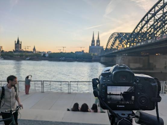 Digitalkamera im Vordergrund, in der Mitte der Rhein, am Horizont der Kölner Dom und rechts die Hohenzollernbrücke