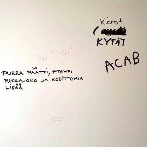 Valkoinen seinä, johon on kirjoitettu eri kynillä ja käsialoilla tekstejä, jotka kritisoivat Riikka Purraa ja poliiseja. Esim. "Kierot kytät ACAB" ja "Purra päätti, pitempi ruokajono ja kodittomia lisää".