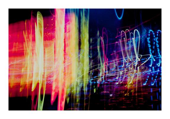 Das Bild ist ein abstraktes Kunstwerk, das durch bewusste Kamerabewegung während der Aufnahme (ICM-Technik) und Mehrfachbelichtung mit etwa einer halben Sekunde Belichtungszeit entstanden ist. Es zeigt ein farbenfrohes Zusammenspiel aus leuchtenden Linien und Flächen. Links dominieren warme Töne – kräftiges Rot, Orange, Pink und Gelb – in vertikal verlaufenden, dynamisch verwischten Bahnen. Sie wirken wie glühende Lichtschleier.

Zur rechten Bildhälfte hin verändern sich die Farben zu kühleren Nuancen: Blau, Violett und Türkis. Hier verlaufen die Lichtspuren in geschwungenen und spiralförmigen Mustern, manche bilden herzähnliche Schleifen. Die Komposition wirkt rhythmisch, vibrierend und erinnert an eine tänzerische Bewegung im Raum – wie visuelle Musik aus Licht.