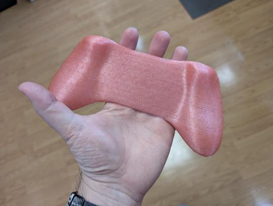 Back side of a 3D printed controller grip, which looks like the back half of a standard console controller like from an Xbox or PlayStation. It's sparkly pink and easily rests in the palm of my hand.