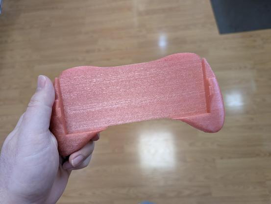 Front view of the same controller grip, which features a big open rectangle in the middle where a handheld console would go. I'm holding it in my left hand, similar to how I would grip when playing.
