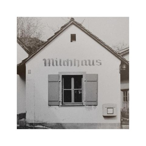 a square black and white image of a tiny house with a gabled roof. on the facade the word "milchhaus" is printed