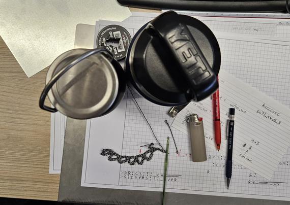 a workspace on graph paper with a lighter, pencil, red pen, green crochet hook, water bottles, steel, and fingernail clippers.