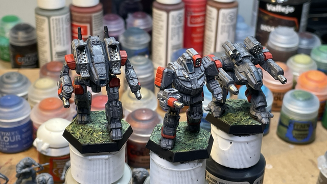 Archer, Wolverine, and Ebon Jaguar miniatures painted grey with red accents