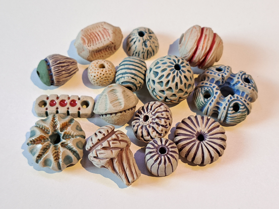 A small pile of pearls, 15 in total, in different shapes and colours. All made out of stoneware clay, with engobes för colour and two with a little bit of glaze.