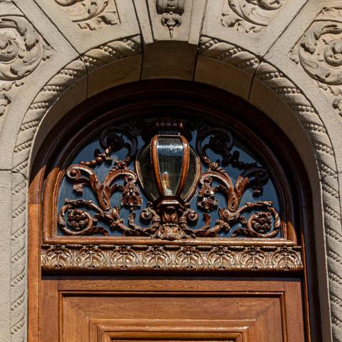 A close-up of the woodwork above the door. Wooden curls and flowers frame a lamp of glass set in wood.