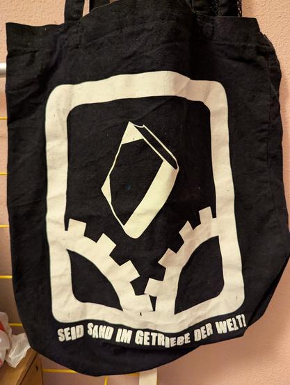 Schwarzer Beutel mit der Aufschrift "Seid Sand im Getriebe der Welt" (Milch und Blut)