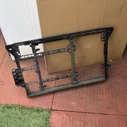 The old black plastic carrier for the A/C condenser and transmission and power steering coolers, removed from the engine compartment of my 2003 BMW 5-series station wagon and leaning against a large cardboard box in front of my open garage door.