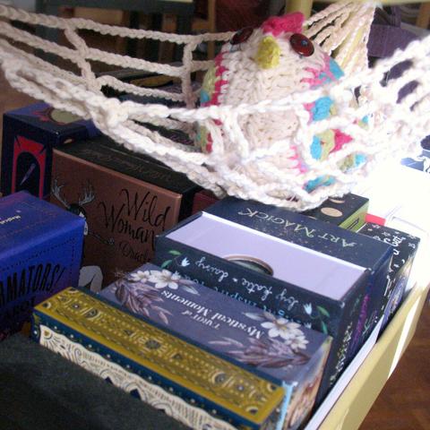 Another bigger granny square chicken (named Elsie) rests in a crochet hammock that looks like a big spiderweb and hangs inside an ikea cart with tarot and oracle decks stored inside.