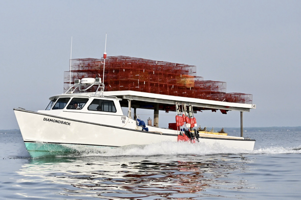 Dead rise workboat with red crab pots on top on the water.