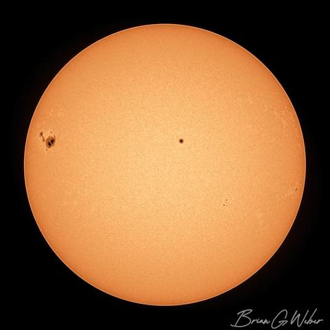 Massive sunspot continuing to rotate into view from the left, while a single large spot dominates the upper middle and tiny spots dot the lower right.