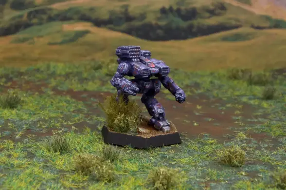 A painted miniature of a Howler 'Mech.  It is painted in a predominantly purple camo pattern with dots of lighter purple and rust red.  The cockpit glass is pink.  The miniature is based to look like it is stepping through heavy brush.  The miniature is photographed on grassy terrain.