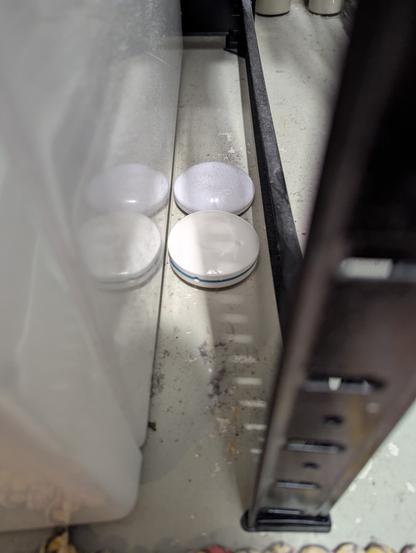 Neben einer Waschmaschine stehen auf dem Boden zwei flache weiße diskusförmige Teile mit etwa 7 cm Durchmesser.