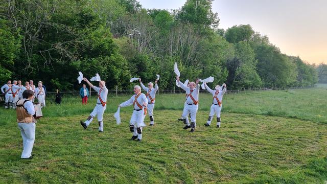 Hanky wielding Morris dancers in a mown patch of a grassy field. The pitch is a bit bumpy.