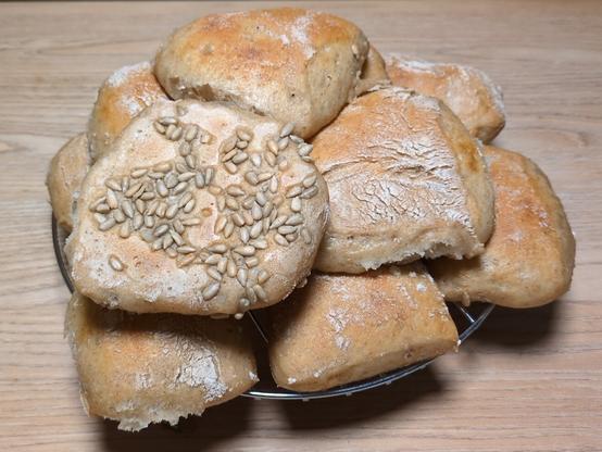 eher flachere Brötchen auf dem Auskühlrost. die Brötchen sind leicht mit Roggenmehl bestaubt. Einige haben Sonnenblumenkerne auf der Unterseite.