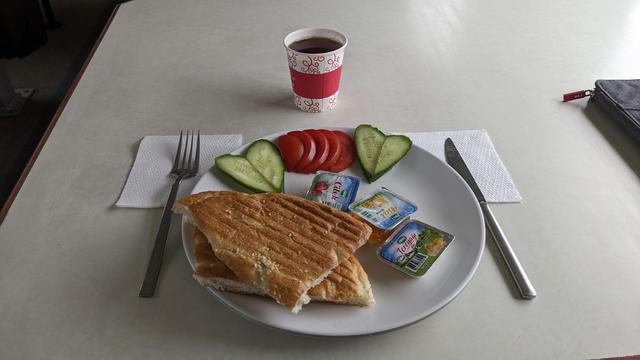 A cup of tea and a plate with bread, jam and some vegetable slices.
