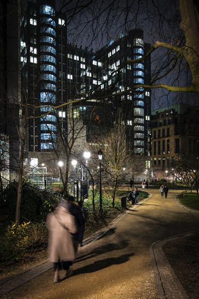 Silhouettes of people going down walking in the Leopold Park in Brussels at night with the illuminated building of the European Parliament in the background.