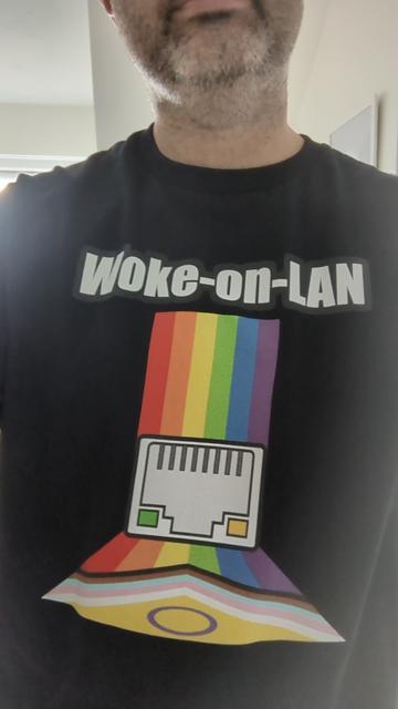 A photo of me wearing a T-shirt saying "woke-on-LAN", with rainbow / LGBT colours and an RJ45 plug