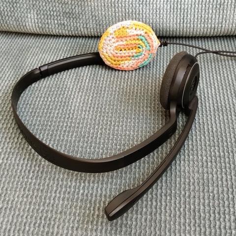 Photo of a typical office headset, one of the earpads replaced with one made of colorful crochet.