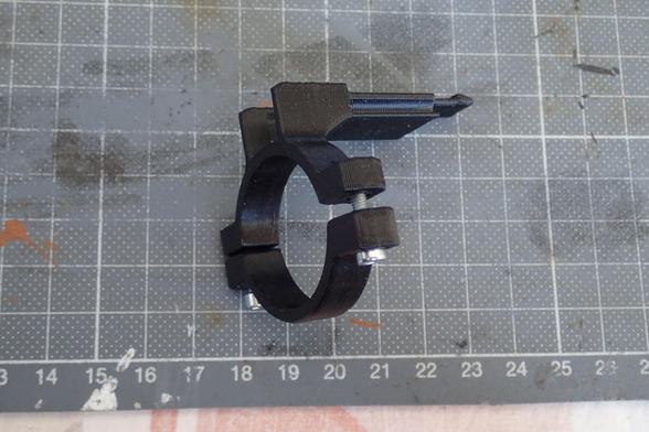 Seitenansicht eines zusammengebauten Displayhalters. Aufbau wie eine Rohrschelle mit Zylinderkopfschrauben an der unteren Halbschale, die Muttern sind in der oberen eingepresst (nicht sichtbar).
Oben rechts, mit einem kleinen Abstand ragt die Schwalbenschwanzschiene nach rechts raus, am Ende befindet sich eine "Schnapplasche", die jedoch nicht genau so funktioniert wie sie ausschaut (drucktechnisch bedingt).