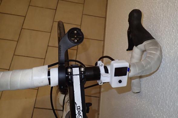 Draufsicht auf einen Rennradlenker mit montierter Halterung für einen Fahrradcomputer und zum rechten Lenkerband hin ein montiertes Display für den OpenBikeSensor. Halterung und Gehäuse sind in weiß gehalten, so wie das (schon verschmutzte) Lenkerband.
Das Display auf der Schwalbenschwanzschiene ist etwas nach rechts versetzt und befindet sich damit schon über weißen dem Lenkerband.