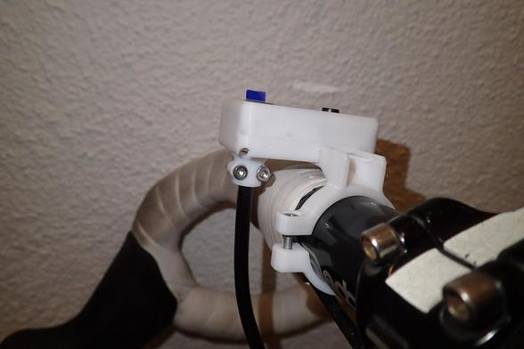 Seitliche Ansicht auf einen Teil des Rennradlenkers mit montiertem Display für den OpenBikeSensor. Halterung und Gehäuse sind in weiß gehalten, so wie das (schon verschmutzte) Lenkerband.

Das Display weist durch Erhöhung der Schwalbenschwanzschiene in der Höhe ein paar Millimeter Abstand zum Lenkerband auf. Somit kann das Display auch über den Lenkergriff (z.B. Gummigriffe wie bei Mountainbikes und Citybikes) bzw. Lenkerband bei Rennrädern montiert werden.

Ebenso sieht man den Knopf des taktilen Drucktasters nur wenige Millimeter aus dem Displaygehäuse ragen.
Auf der linken Seite des Gehäuses (=in Fahrtrichtung) ragt die Kabel-Zugentlastung mit samt dem Kabel raus aus dem Displaygehäuse. Das Kabel weist ausreichend Abstand zum Lenker samt Lenkerband auf.