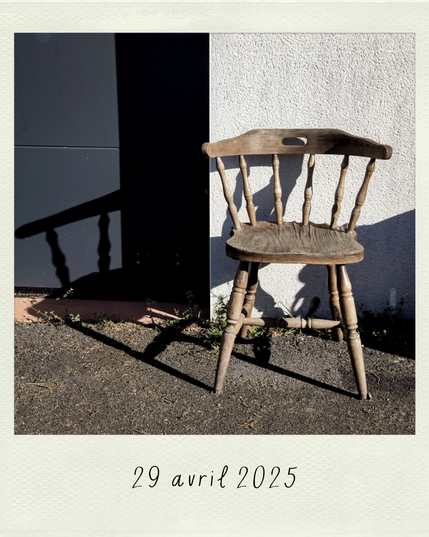 un fauteuil en bois devant un mur blanc, son ombre se projetant à gauche, sur un mur gris foncé
