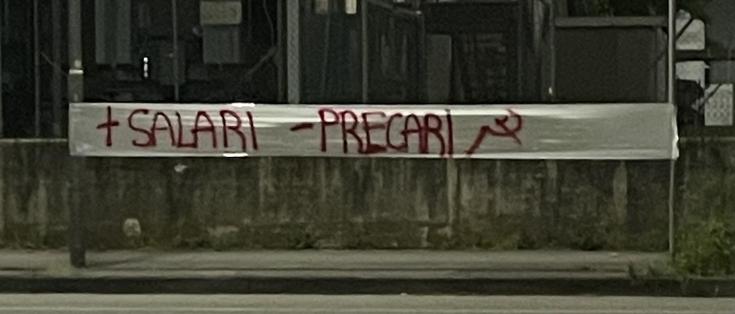 Striscione appeso in Zona Industriale a Padova con su scritto: “ + salari, - precari “ con falce e martello a fianco.
