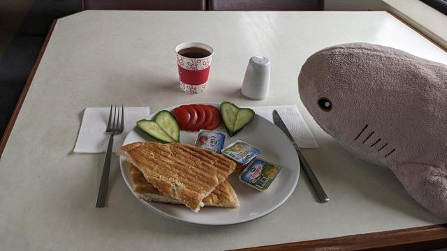 Rosåhaj in a dining car looking at a plate with bread, jam and vegetables.