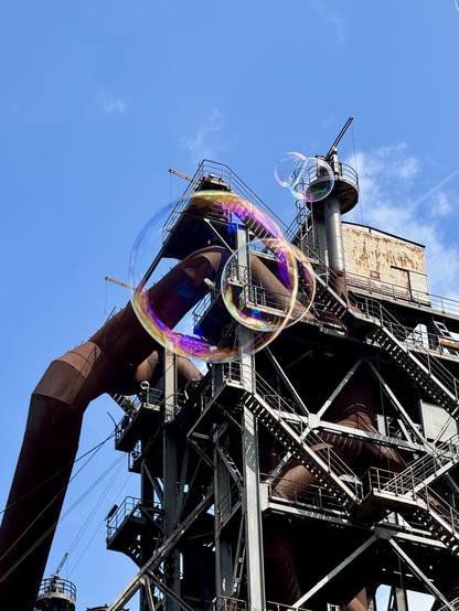 grossaufnahme von schillernden seifenblasen vor rostiger industrieruine und strahlend blauem himmel