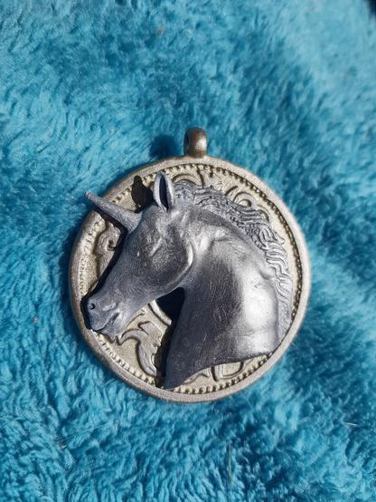 Un pendentif doré orné d'une tête de licorne argentée.