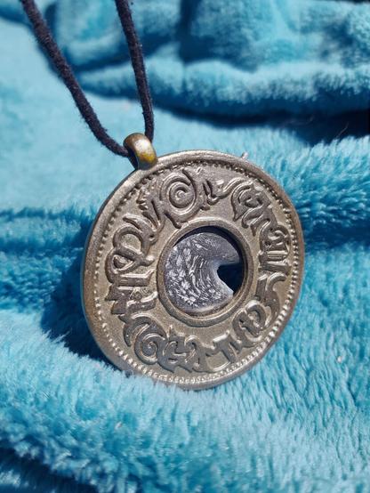 Un pendentif doré orné d'une tête de licorne argentée (mais là c'est de dos donc la tête est cachée par le médaillon).