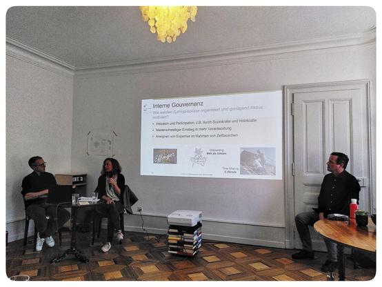 Two presenters sitting, with a slide about Governance, and Matthias from Urbane Dörfer in the audience.