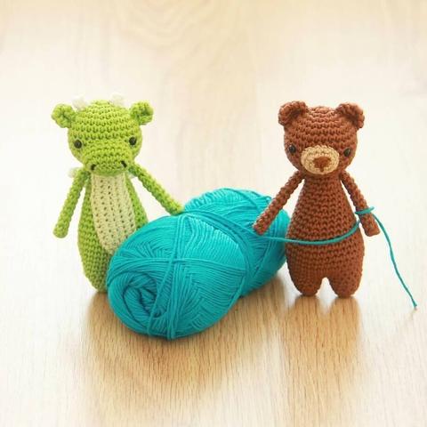 Picture of two small crocheted amigurumi animals, a green dragon and a brown bear. They're standing next to a blue skein of cotton yarn.