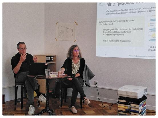 Two authors explaining a key concept from their book, next to a slide presentation