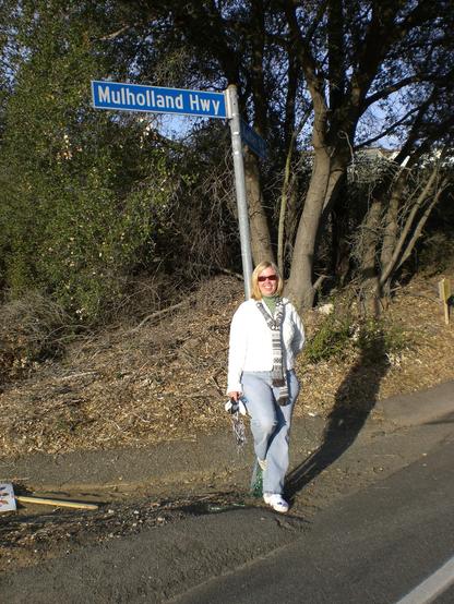 A woman leans against a sign post asking Mulholland Highway.
