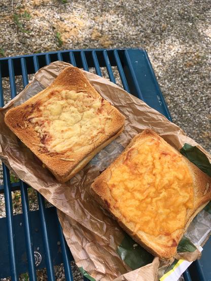Deux croque-monsieur posés sur un banc. Enfin... techniquement, il sont posés sur un cornet (on dit comme ça à Metz !) en papier lui-même posé sur un banc.
L'un est recouvert d'un peu de béchamel et de Comté. L'autre est au cheddar.