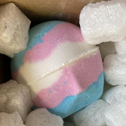 Close up of a Lush “Liberation” bath bomb which is made up of the stripe colours of the trans pride flag. Blue > pink > white > pink > blue.