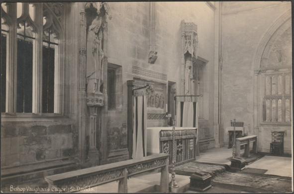 Monochrome real photographic postcard showing a view of Bishop Vaughan's Chapel in St David's Cathedral in Pembrokeshire.

Published by Mendus, Chemist, St David's, not numbered, large view, 146 x 96 mm, c.1930s.

Postally unused.

Very good condition, with very slight corner bumps, but slight yellowing.