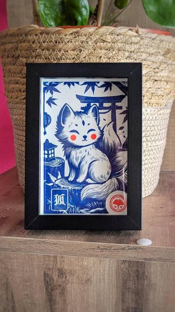 Kawaii illustration in a black frame depicting a stylized kitsune fox with red cheeks and multiple tails, sitting beside a lantern and tree stumps under maple leaves with a torii gate in the background; includes Japanese characters and a red circular emblem.