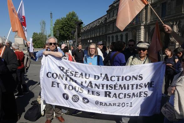 Photo de militant·es du RAAR tenant une banderole blanche avec le nom de l'association et des drapeaux aux couleurs du RAAR.