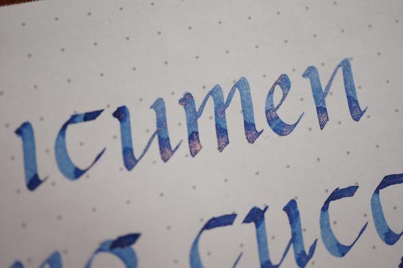 "icumen" in periwinkle ink with gold glitter, written in Carolingian minuscule